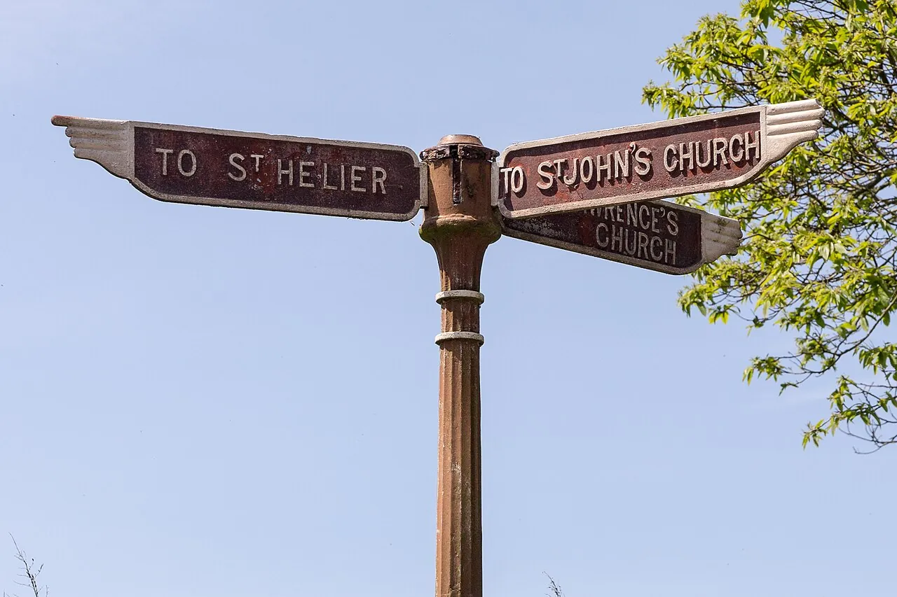 Чугунный указатель-палец с надписями To St Helier и To St John's Church на фоне голубого неба